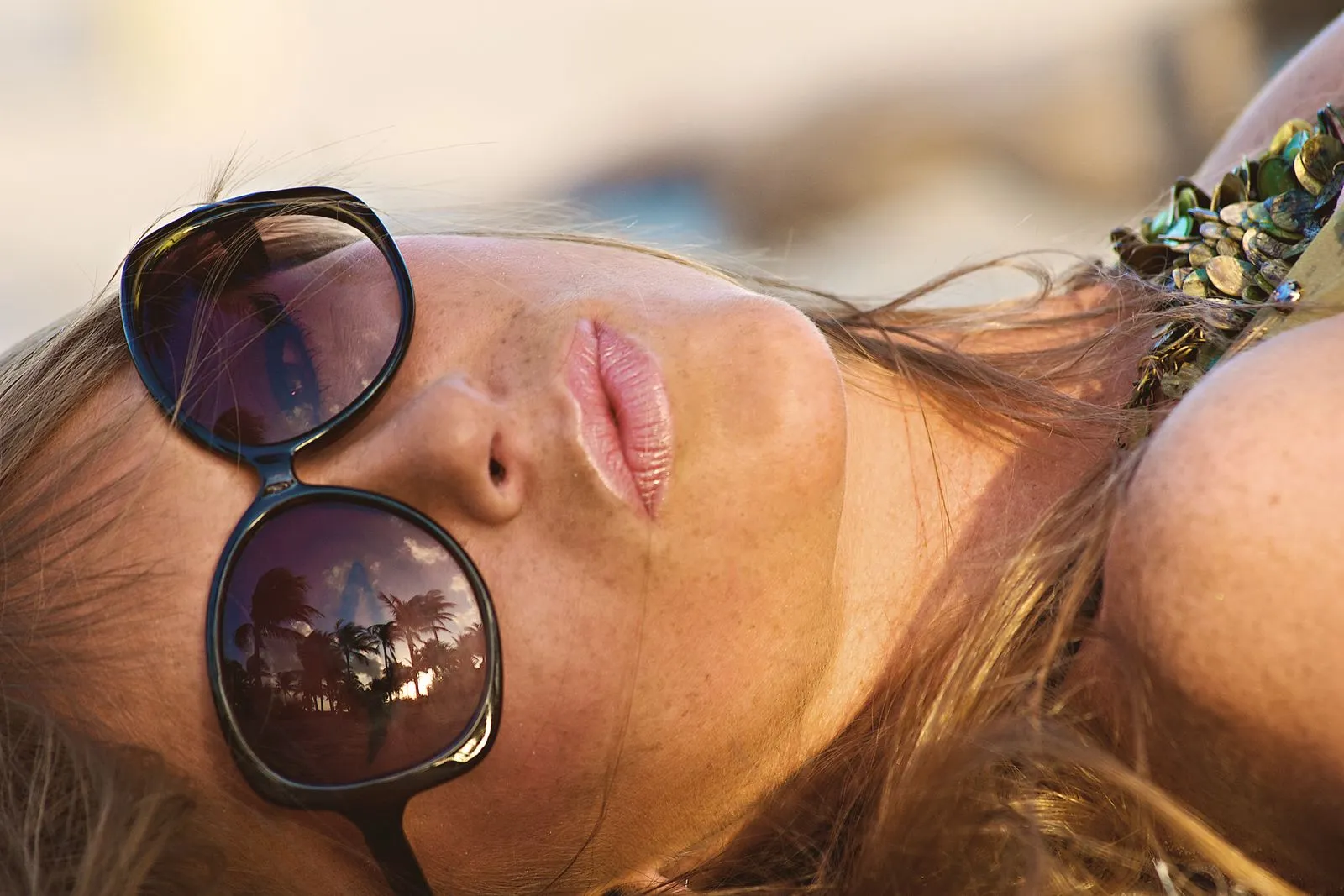 Close-up of a woman relaxing with palm tree reflections in sunglasses at Miami Beach.